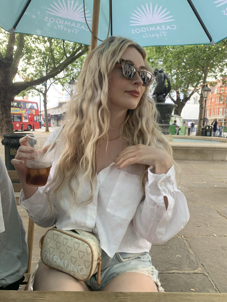 Girl in Sloane Square, Chelsea in an outdoor summer bar wearing a white shirt and sunglasses