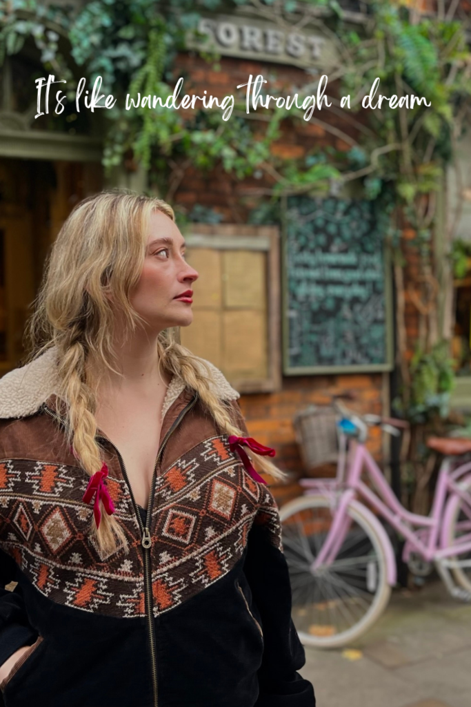 woman with plaits standing outside a cafe with a pink bike 