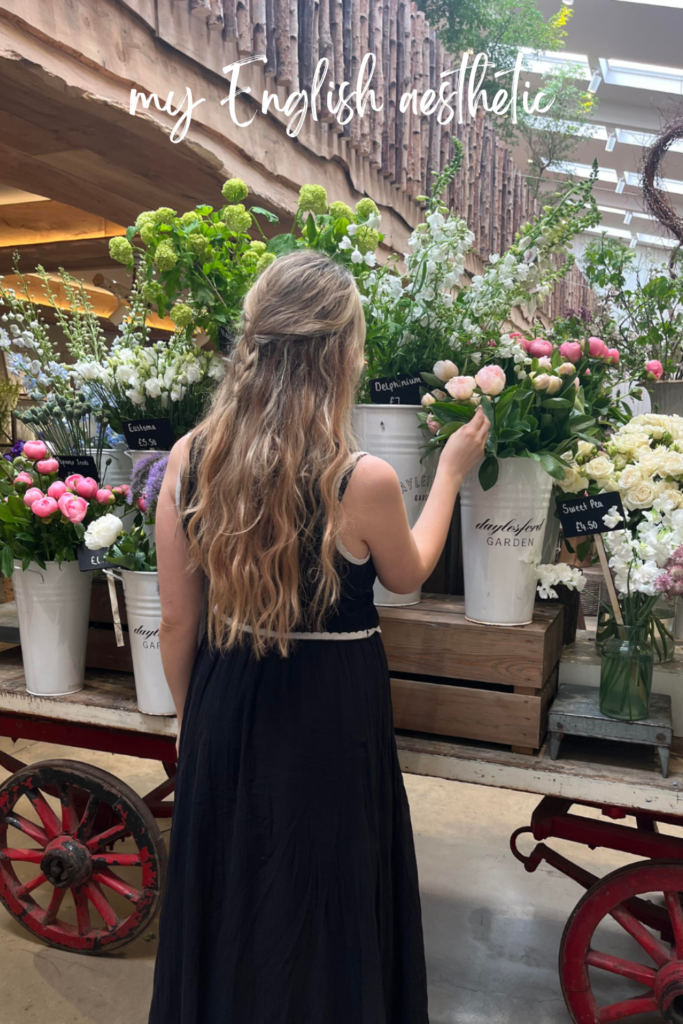 blonde woman in black dress starting at a cart of flowers in Daylesford farm shop