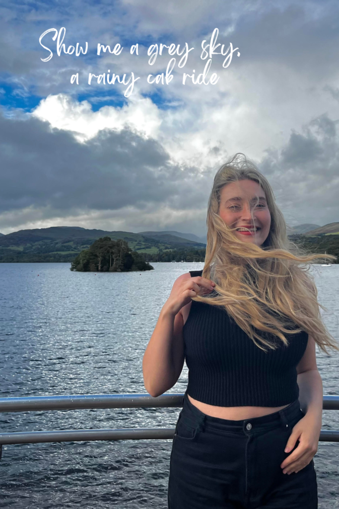 blonde woman on a boat on windermere lake laughing in the wind with grey skies 